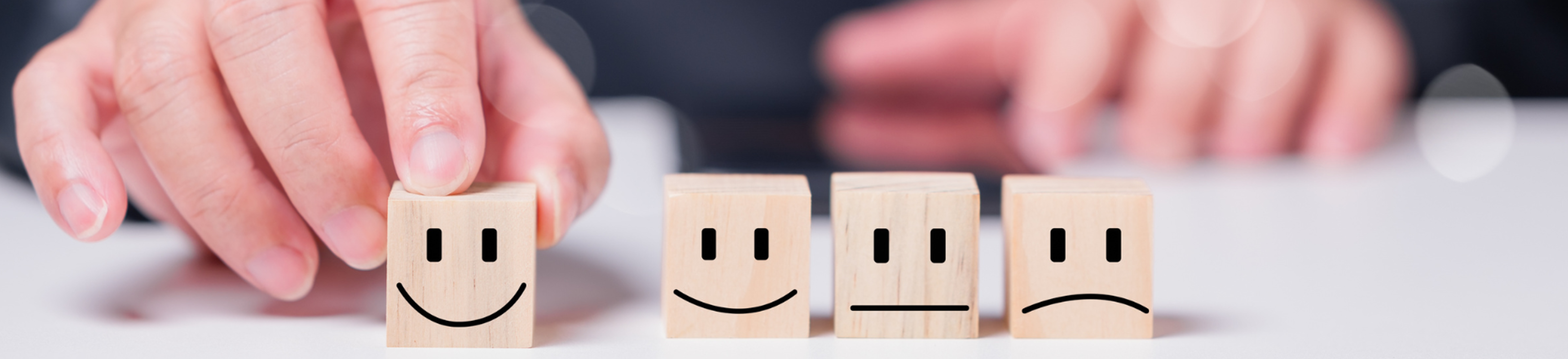 Image of wooden blocks with diffent expressions. 
            A finger points to the one that is smiling.